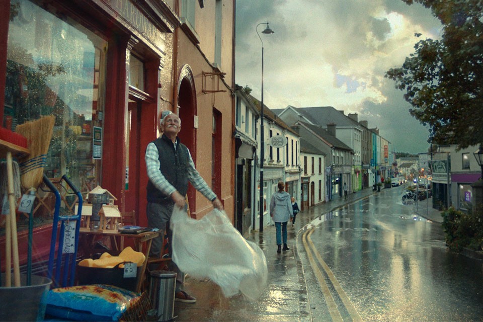 Older man in the rain covering his hardware store stock outside of his shop with a waterproof cover.